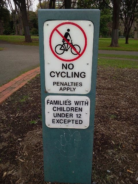 Bicycle warning sign: 'No Cycling, Penalties Apply. Families with children under 12 excepted'